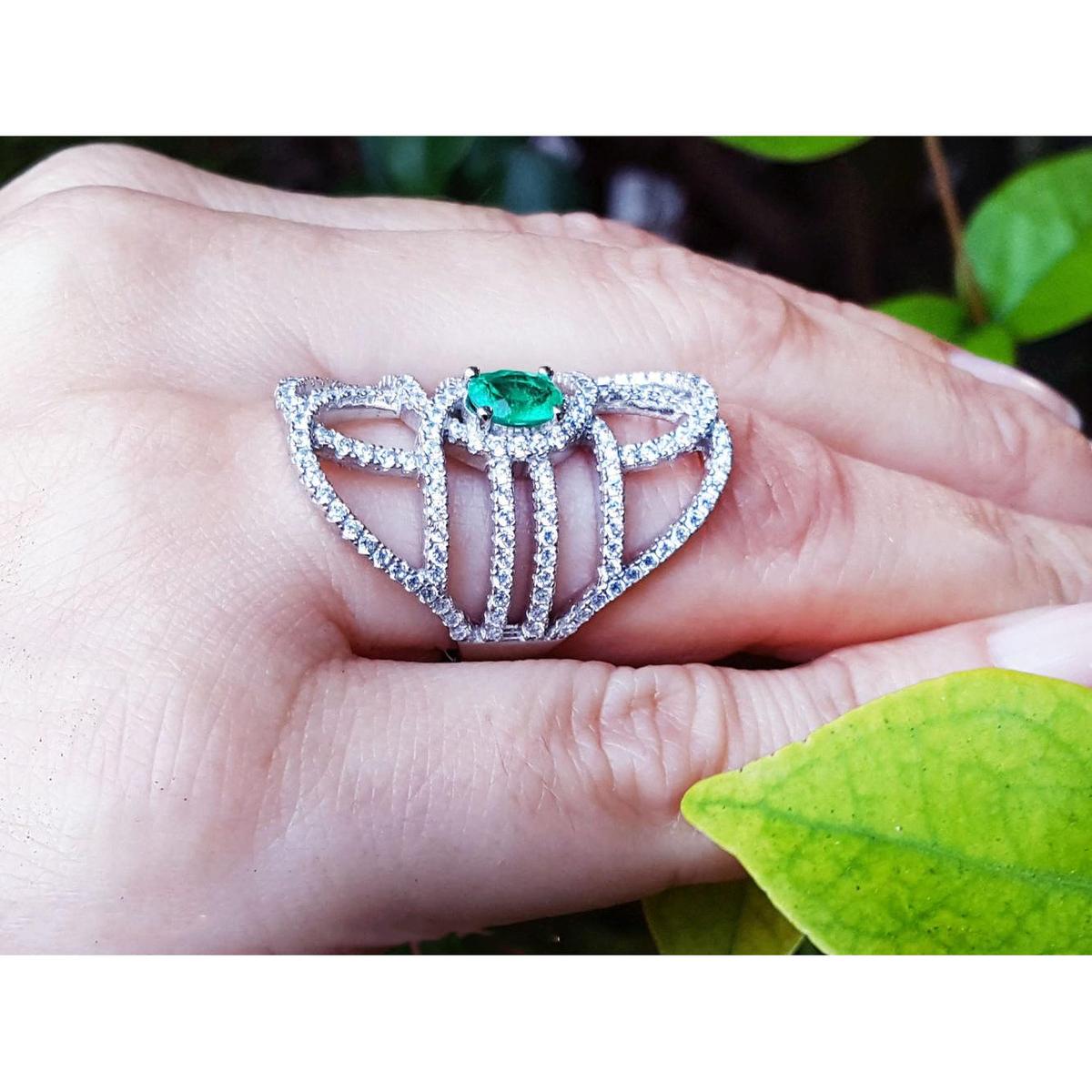 Silver ring with a oval cut natural emerald on a hand with a leaf background.