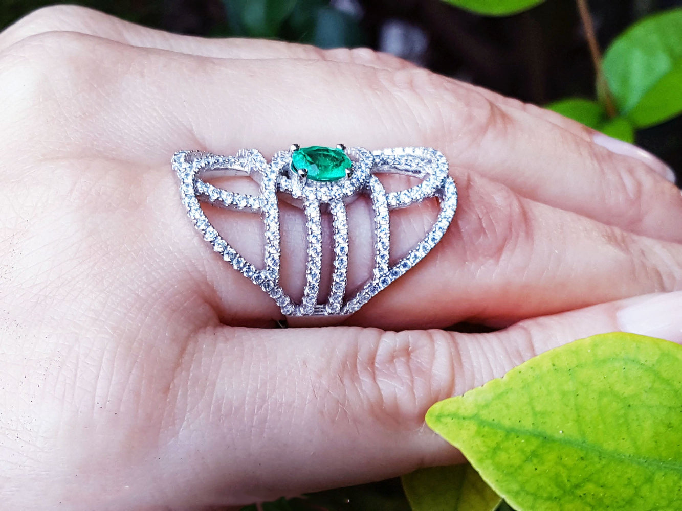 Silver ring with a oval cut natural emerald on a hand with a leaf background.