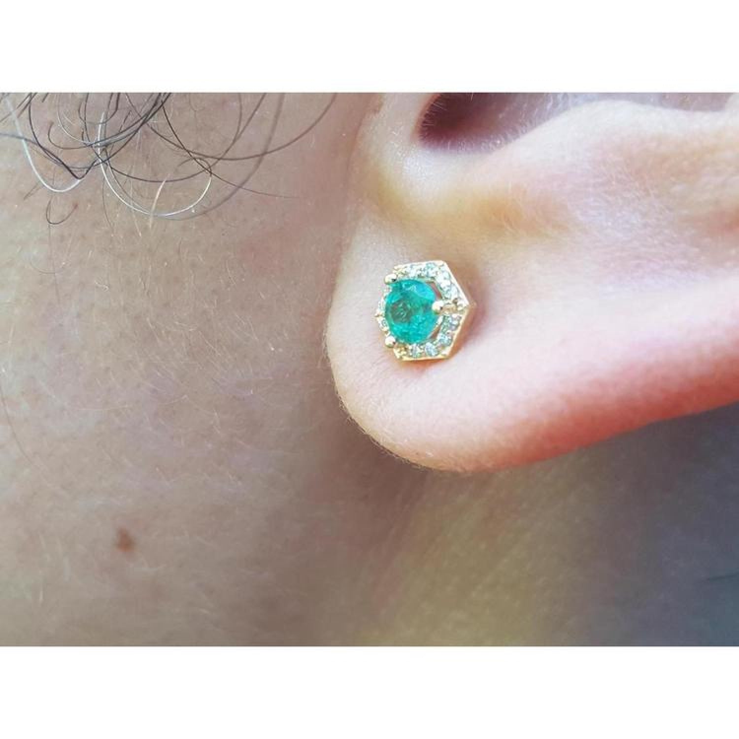 Hexagon emerald and diamond stud earring in 14K yellow gold, worn on an ear.