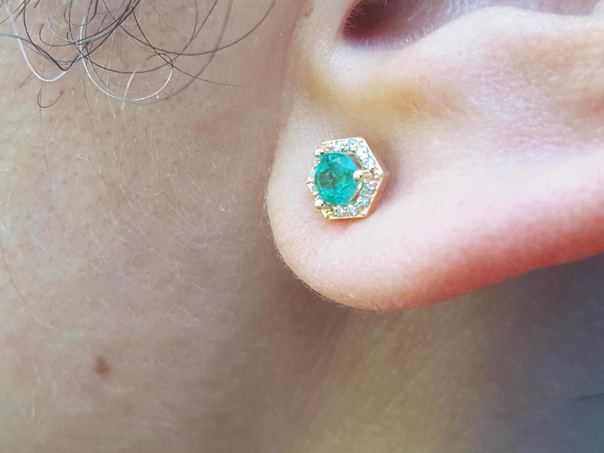 A close up of ear wearing a 14k gold emerald stud earring.