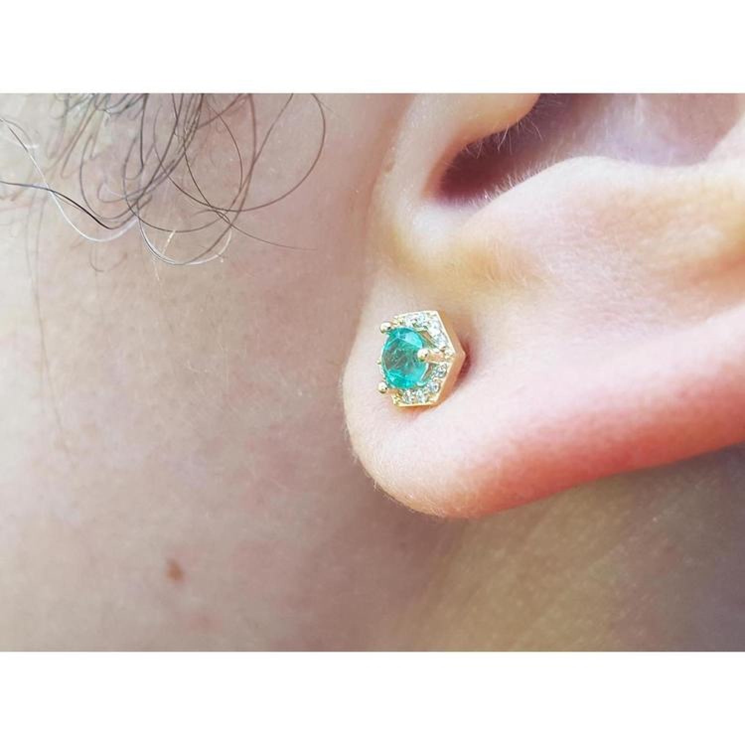 Hexagon emerald and diamond stud earring in 14K yellow gold on an ear.