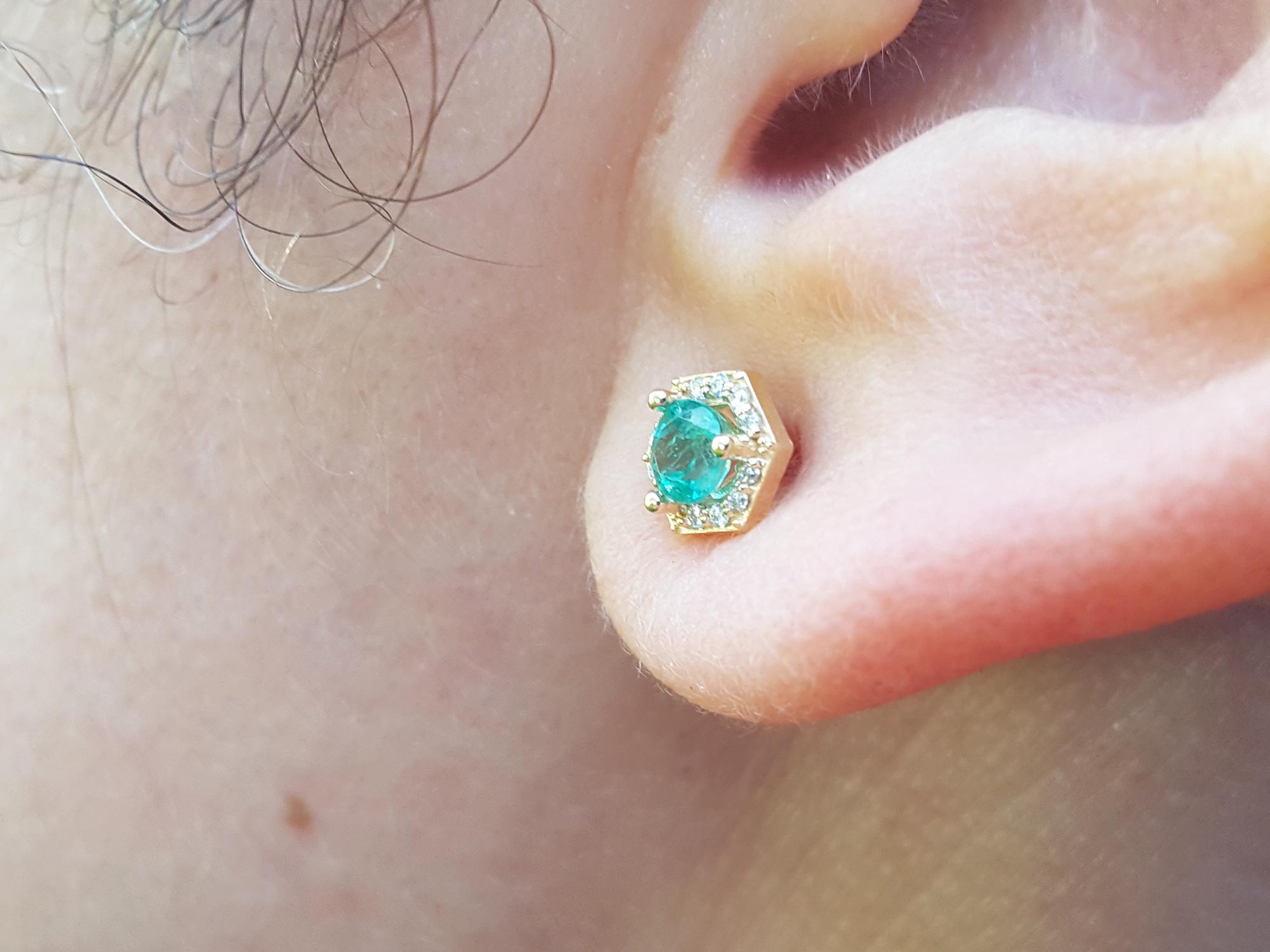A closer vie of an earlobe wearing a yellow gold emerald stud earring.