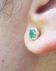 A closer vie of an earlobe wearing a yellow gold emerald stud earring.