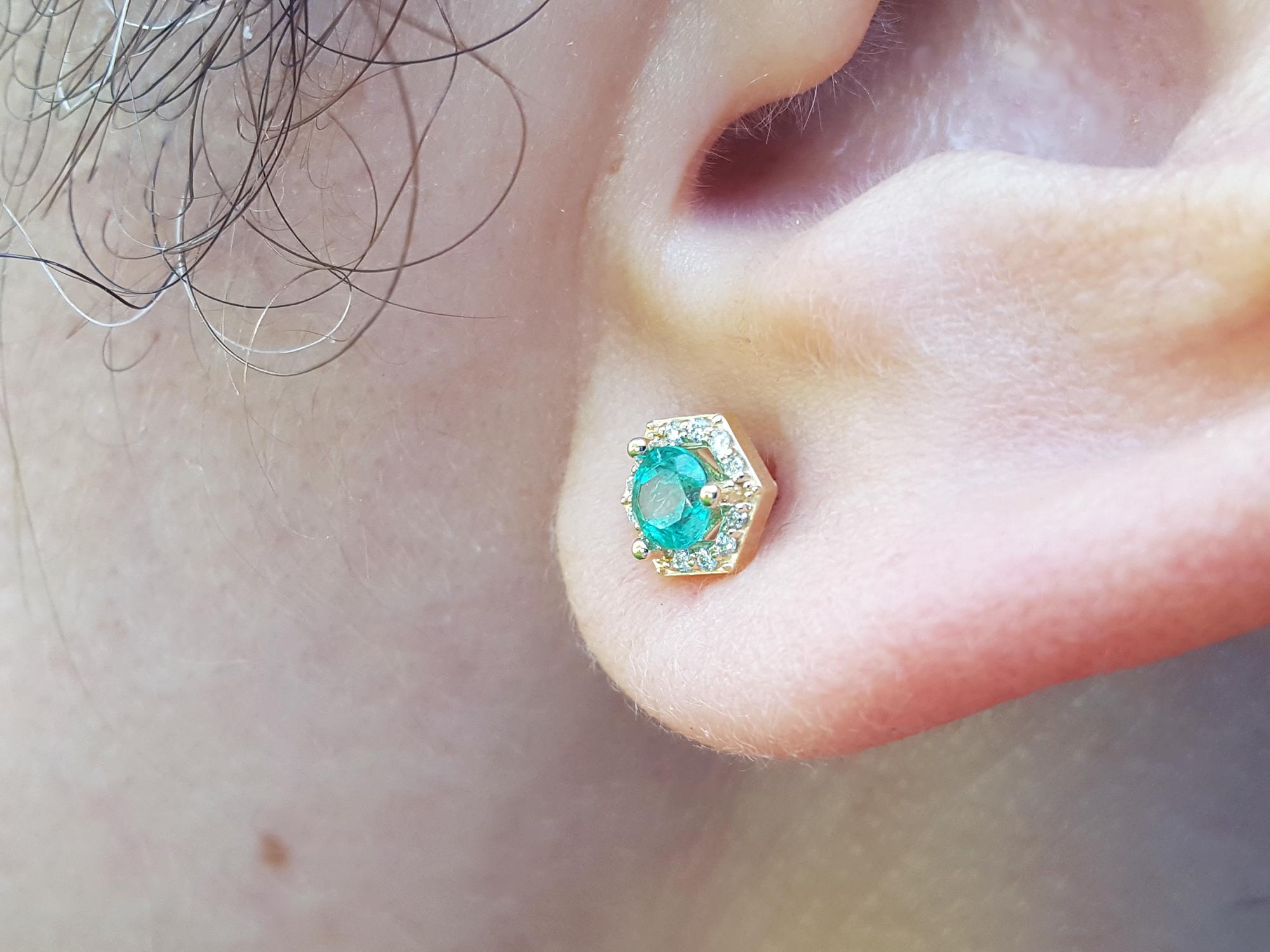 An earlobe waring a emerald stud earring yellow gold.