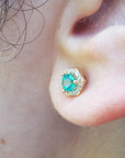 An earlobe waring a emerald stud earring yellow gold.