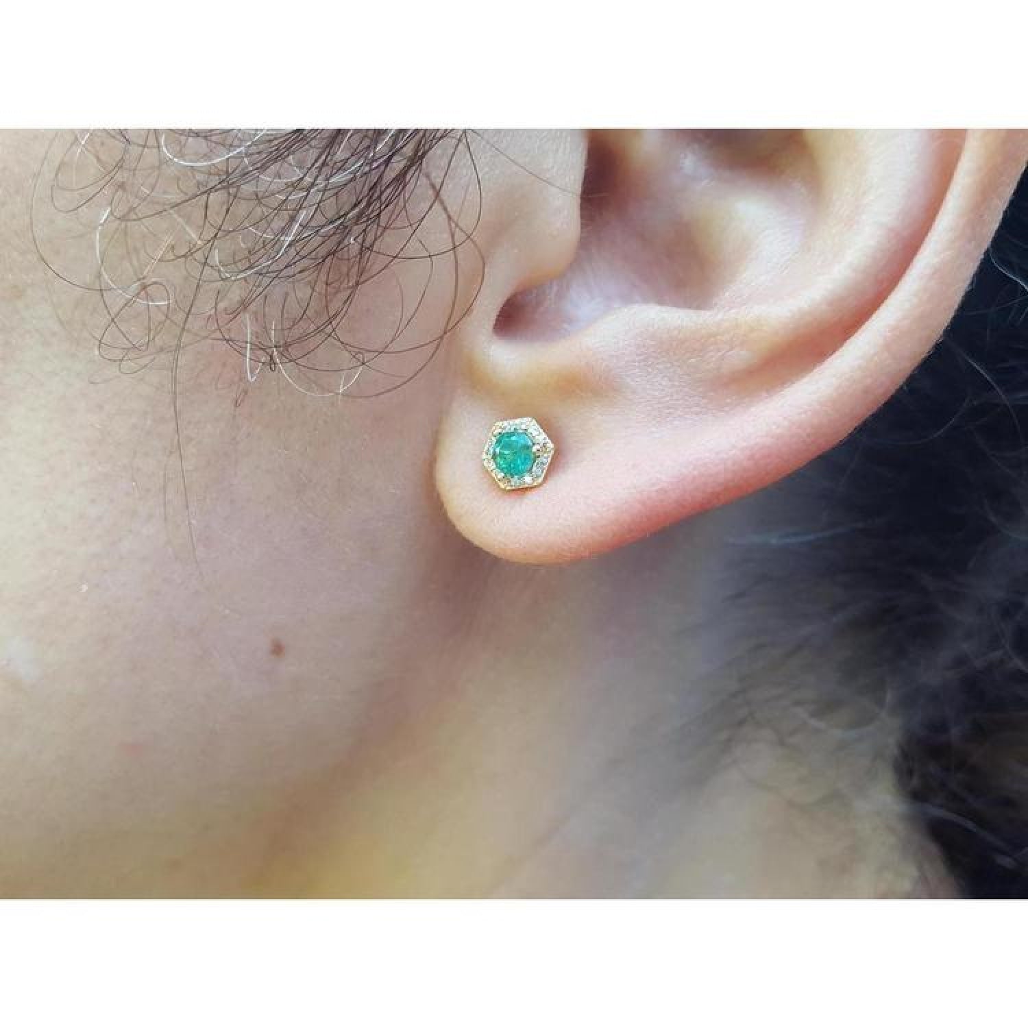 Hexagon emerald and diamond stud earring in 14K yellow gold on an ear.