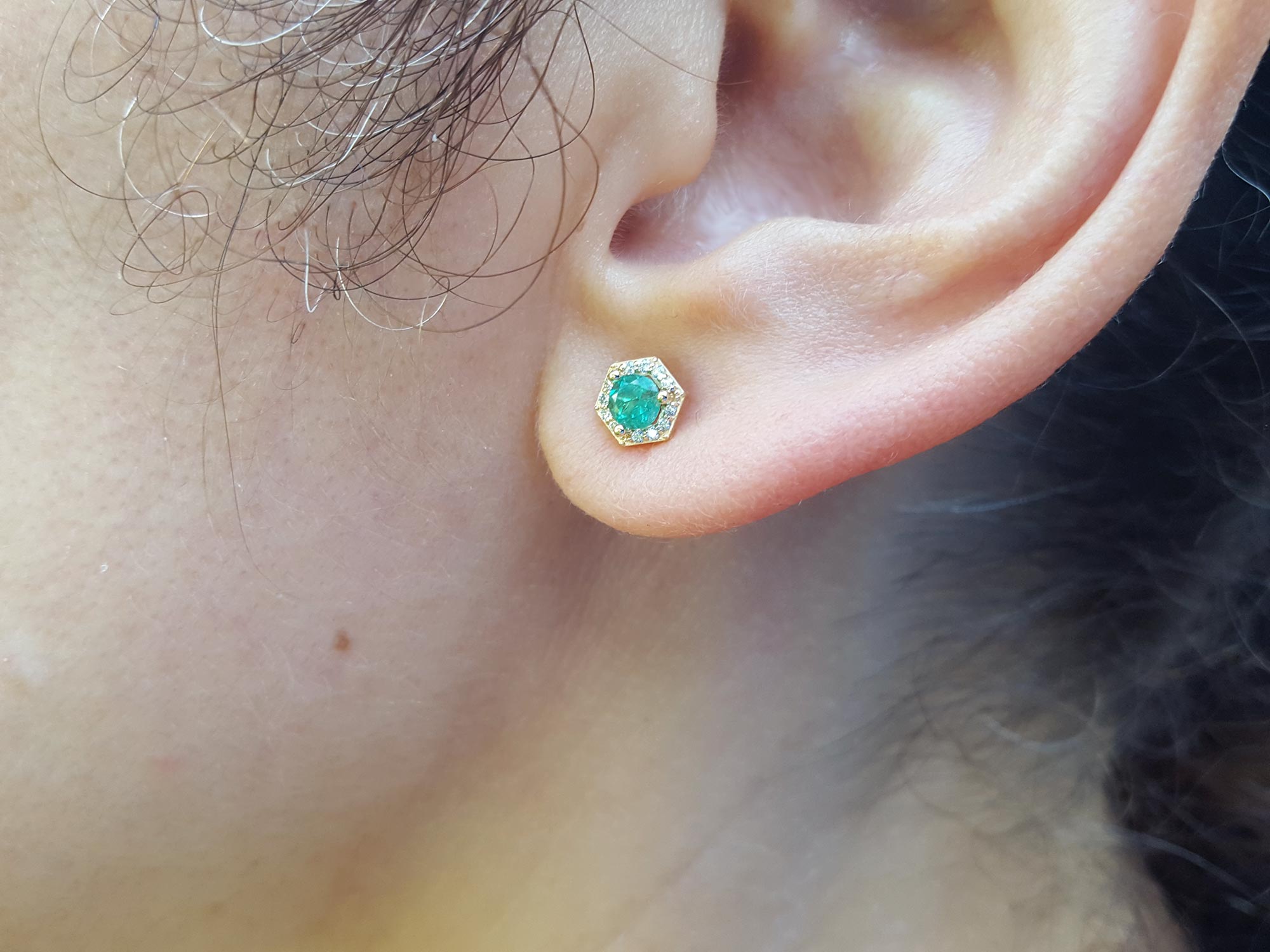 A woman&#39;s ear dressing an hexagonal emerald stud earring yellow gold.