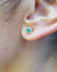 A woman's ear dressing an hexagonal emerald stud earring yellow gold.