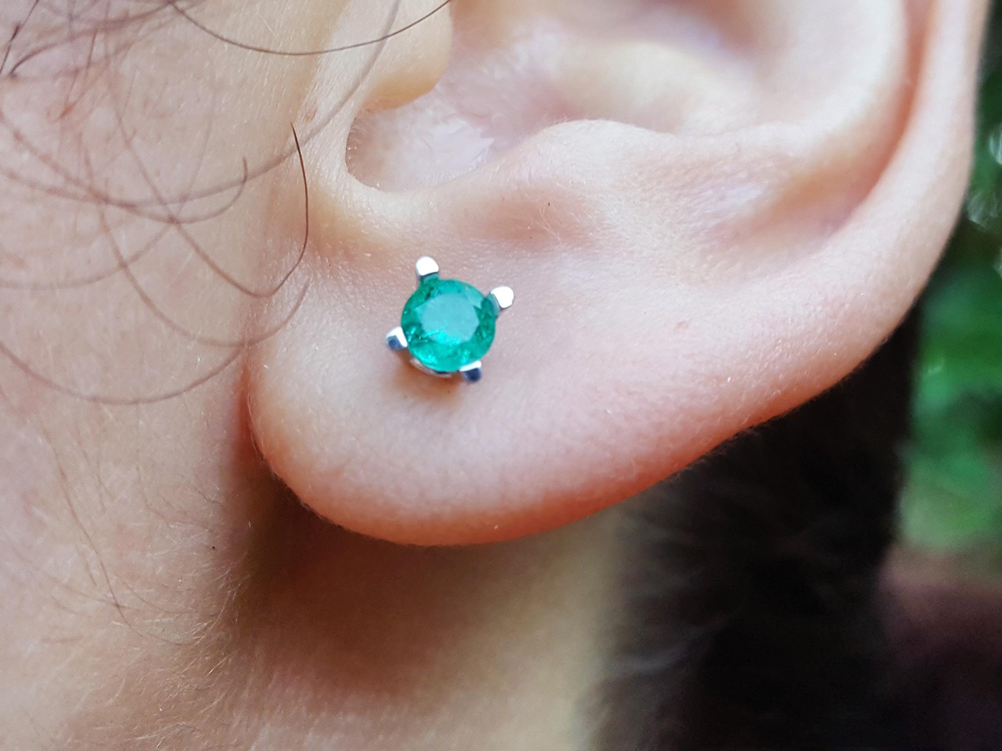 Close-up of an ear with a round cut emerald stud earring.