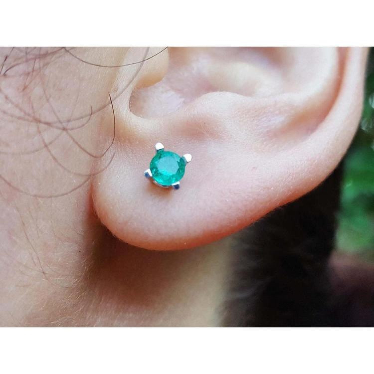 Close-up of an ear with a round cut emerald stud earring four prong setting in 1k yellow gold.