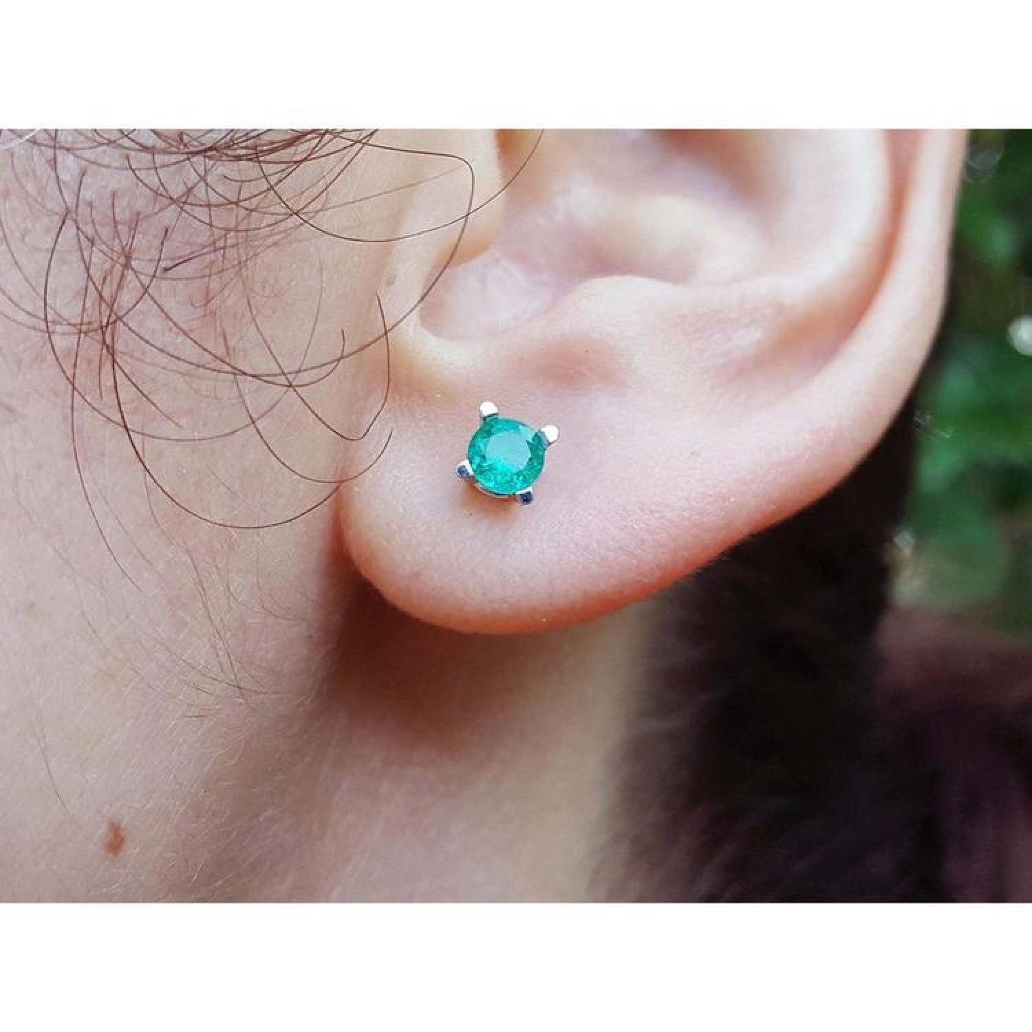 Close-up of an ear wearing a emerald gemstone earring with a blurred natural background.