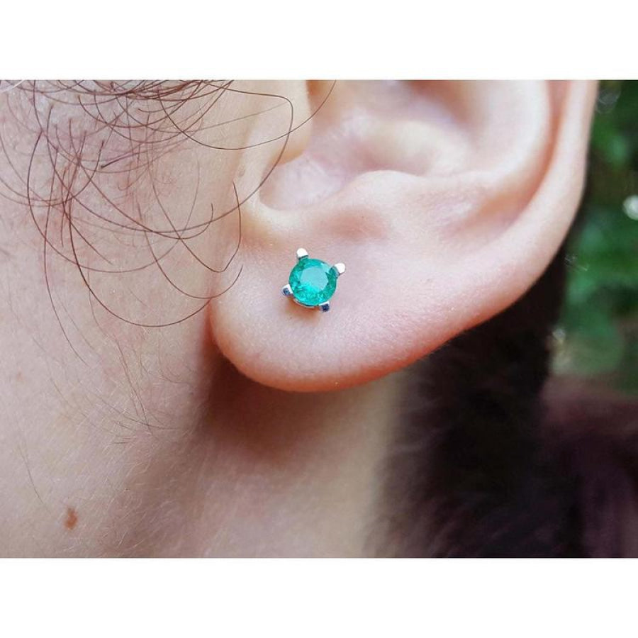 Close-up of an ear wearing a emerald gemstone earring with a blurred natural background.