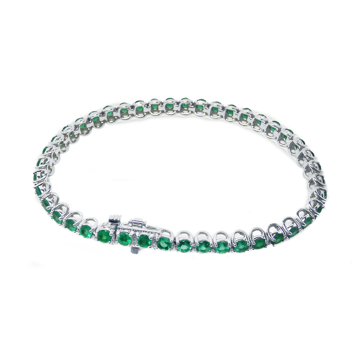 The underside view of a white gold tennis bracelet with emeralds on a white background.