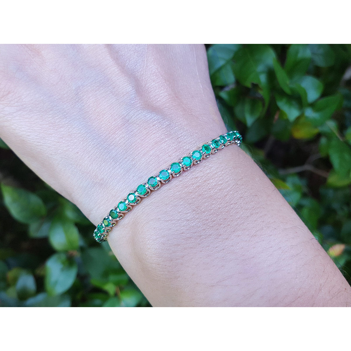 An emerald tennis bracelet on a wrist with a natural background.