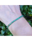 An emerald tennis bracelet on a wrist with a natural background.