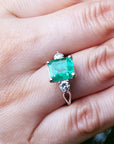 A close-up of a ring with a natural emerald on a hand.