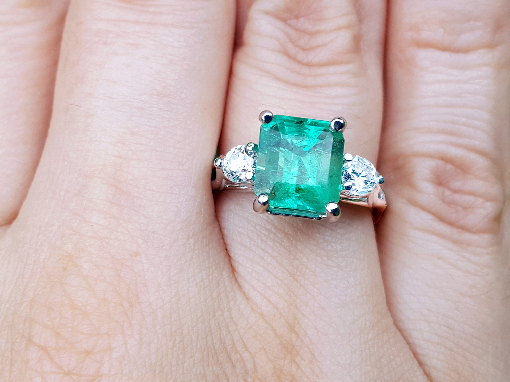 Emerald three stone ring with diamond accents on a finger.