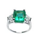 A white gold square emerald ring with side diamonds on a white background.
