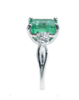 Dainty white gold emerald ring with side diamond and band visibles on a white background.