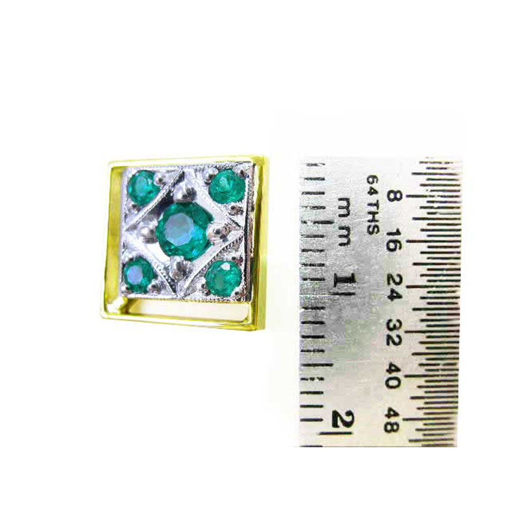 A yellow and white gold emerald cufflink next to a ruler for scale on a white background
