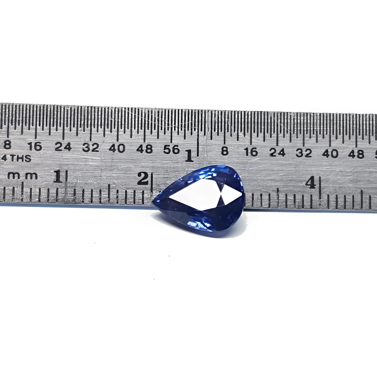Deep blue pear-cut natural sapphire gemstone next to a ruler, showing its size and brilliant facets.