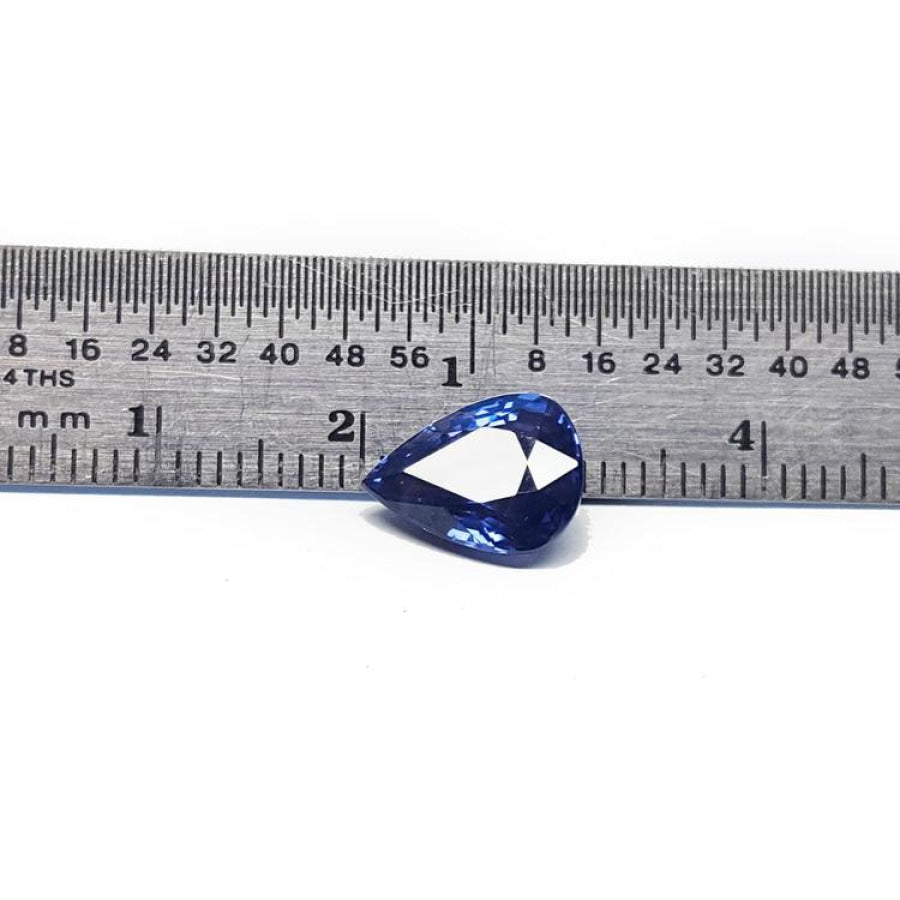Deep blue pear-cut natural sapphire gemstone next to a ruler, showing its size and brilliant facets.