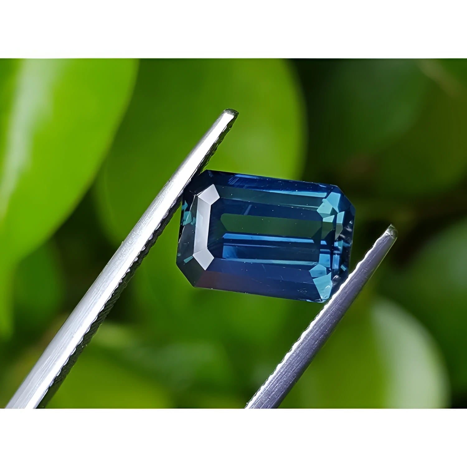 5.05 ct. GIA certified deep blue-green emerald cut sapphire held by tweezers.