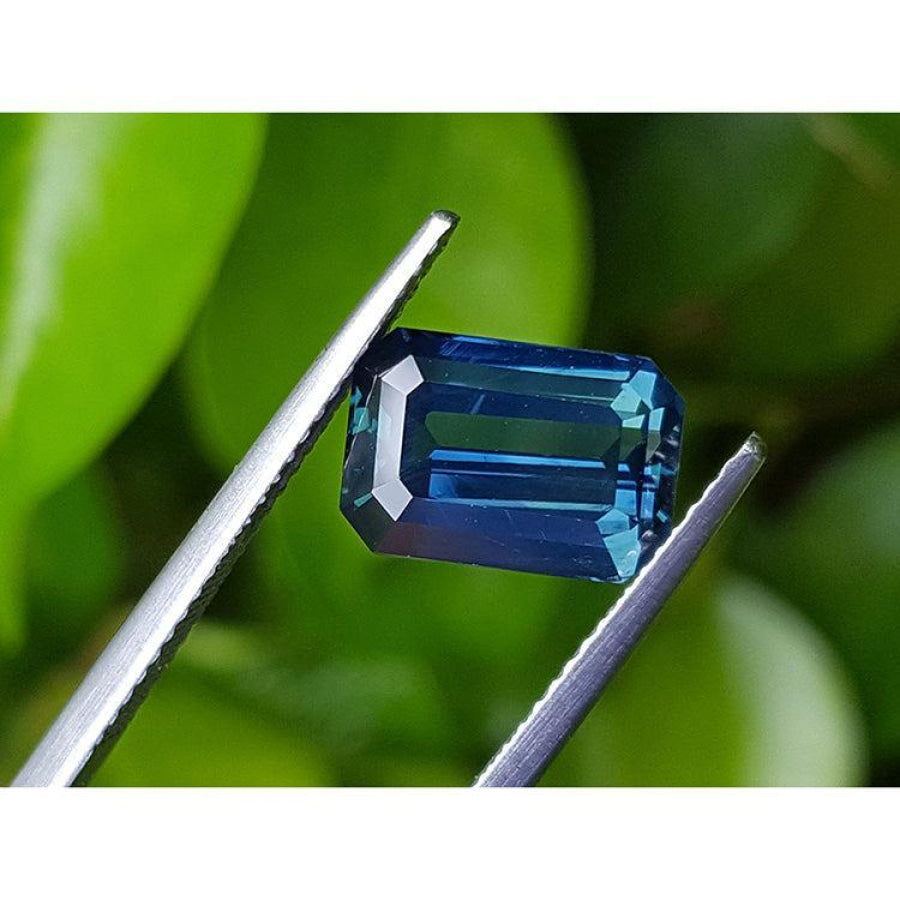 5.05 ct. GIA certified deep blue-green emerald cut sapphire held by tweezers.