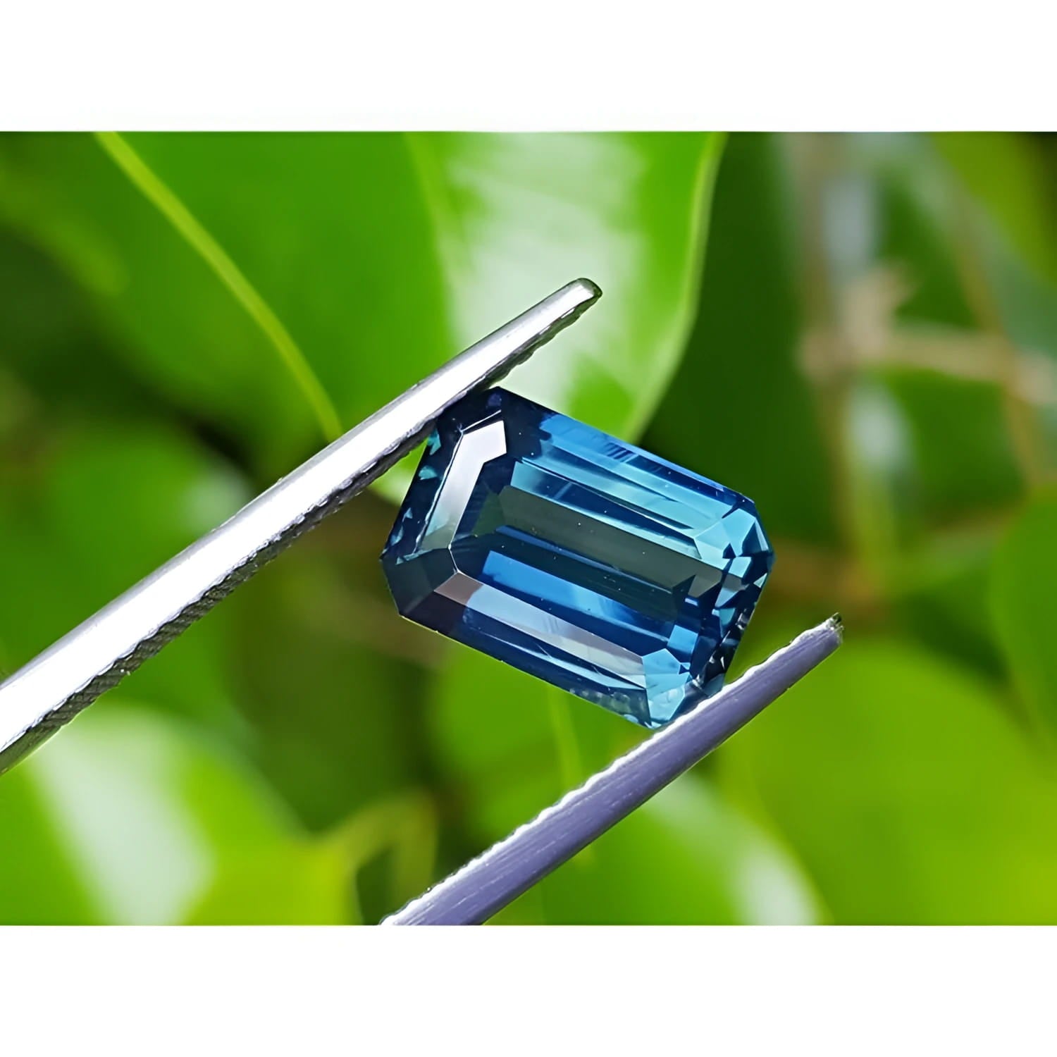 5.05 ct GIA certified deep blue-green emerald cut sapphire held by tweezers.