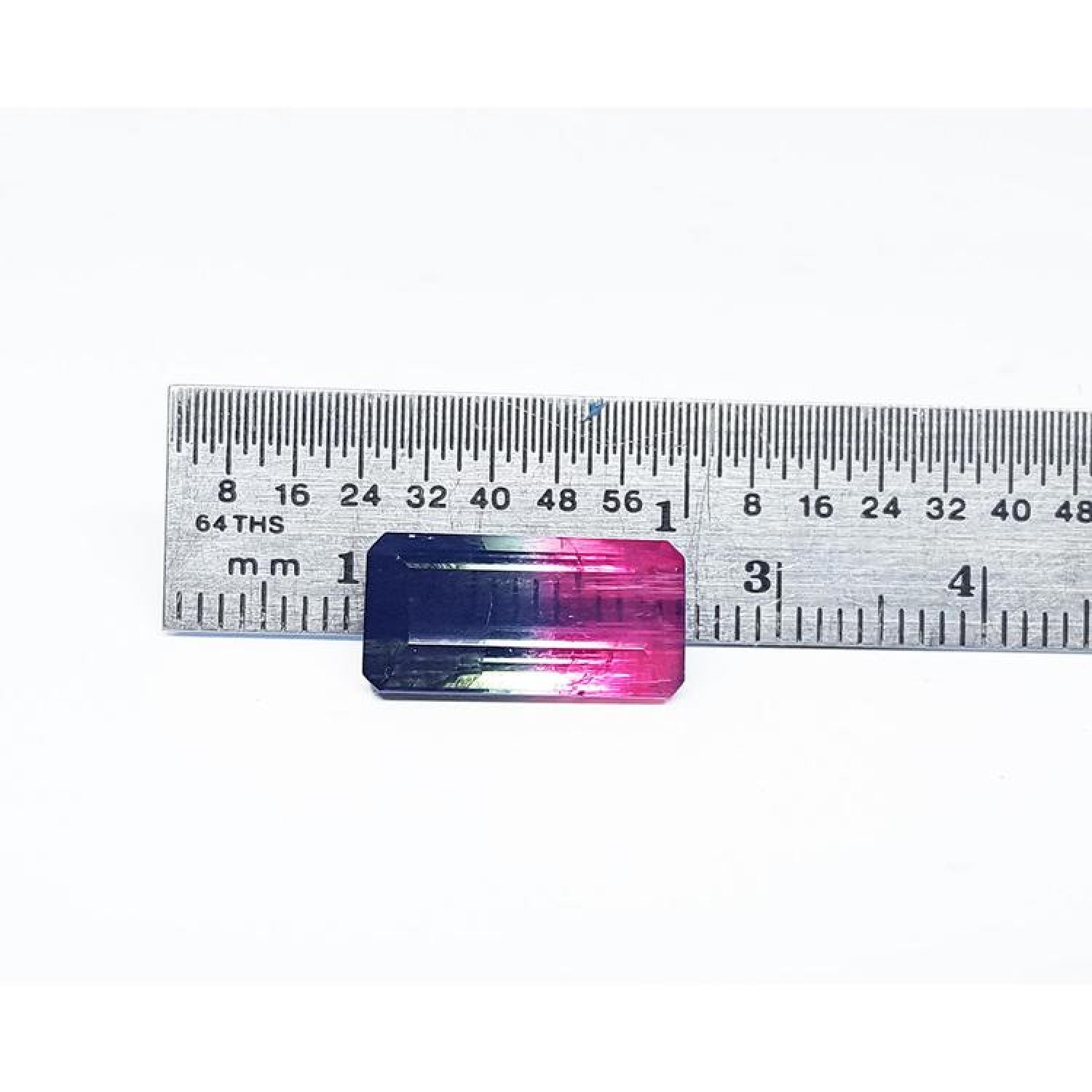 Emerald cut 6.11 ct natural loose watermelon tourmaline with bluish green and red-orange hues, measured against a ruler.