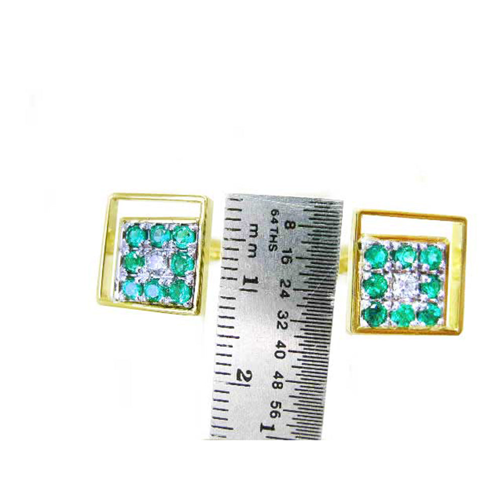 Gold square of emerald cufflinks next to a ruler for size reference on a white background