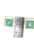 Gold square of emerald cufflinks next to a ruler for size reference on a white background