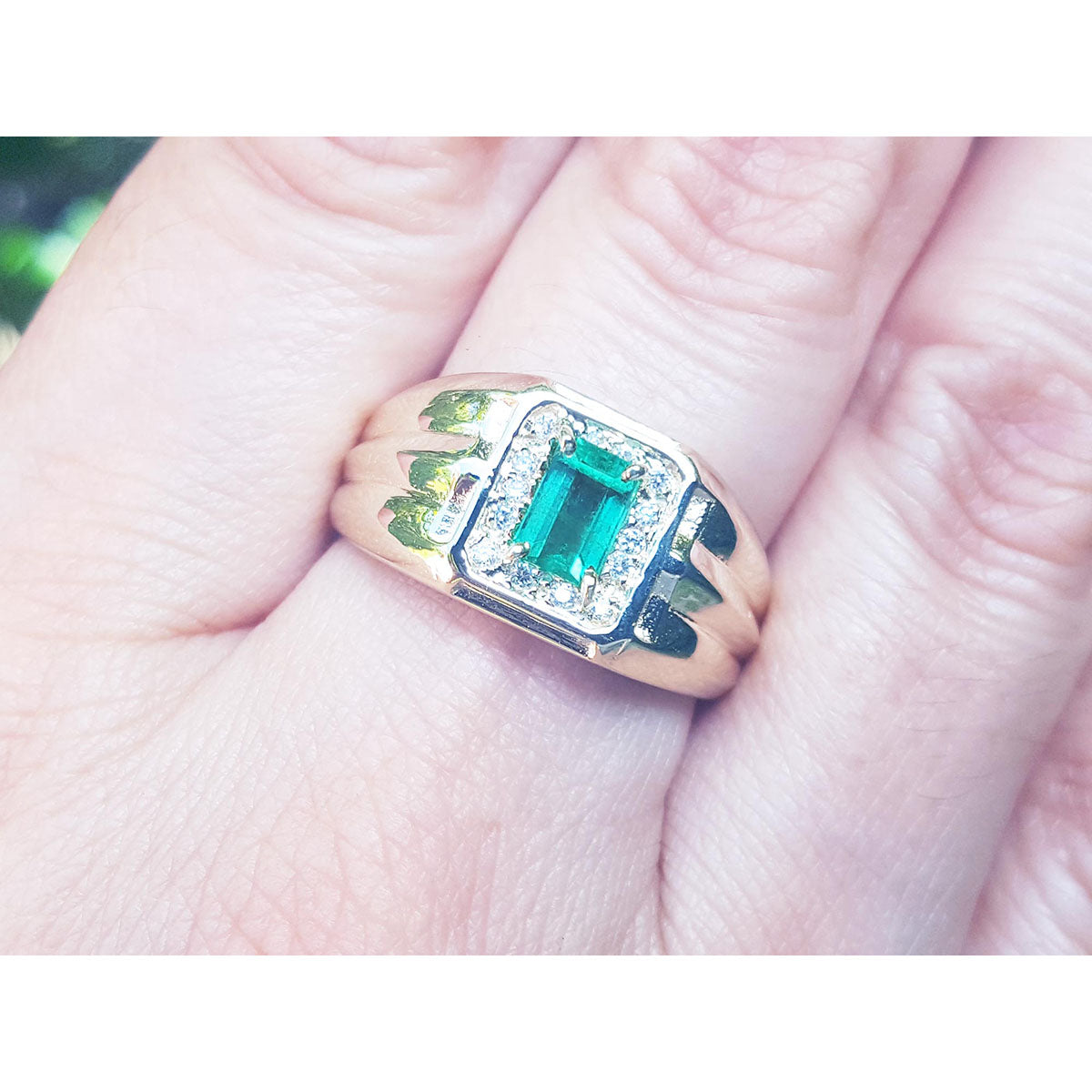 Men's gold ring with a square natural emerald worn between fingers.