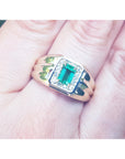 Men's gold ring with a square natural emerald worn between fingers.