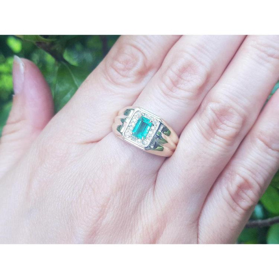Men's 14K yellow gold ring with a rectangular Muzo emerald and diamond halo, worn on a hand.