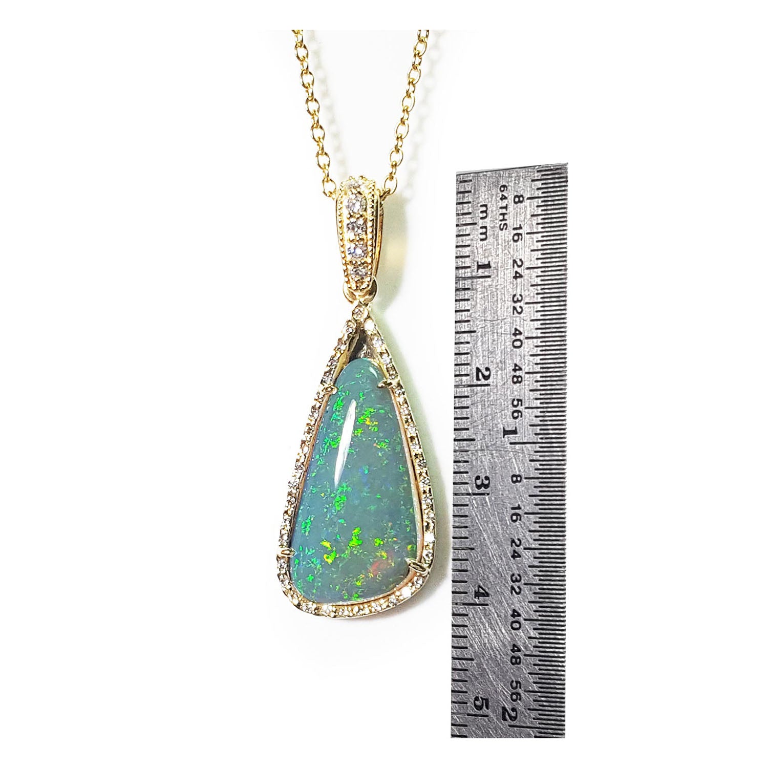 Teardrop-shaped opal pendant on a gold chain with a ruler for scale on a white background