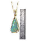 Teardrop-shaped opal pendant on a gold chain with a ruler for scale on a white background