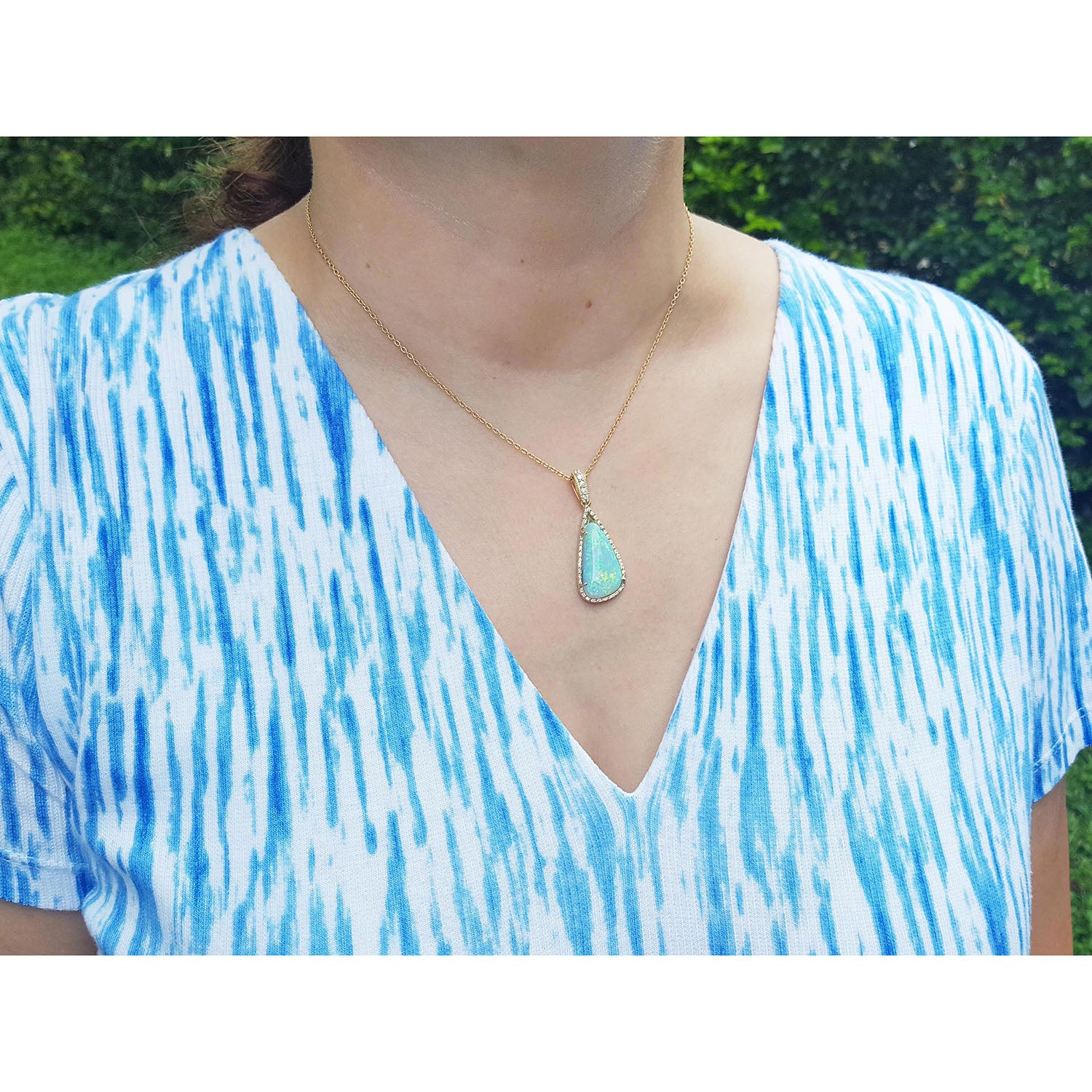 A woman wearing a blue and white patterned top with a gold necklace and natural opal pendant.