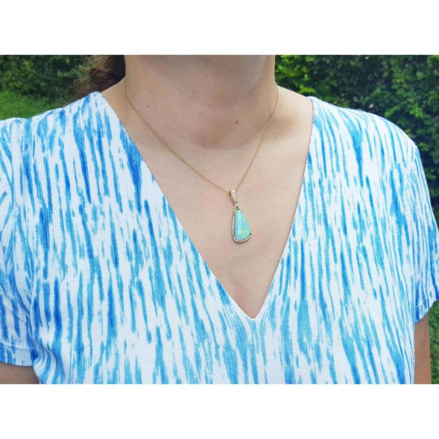 Pear-shaped Australian opal pendant with halo diamonds on an 18K gold chain, worn on a woman.