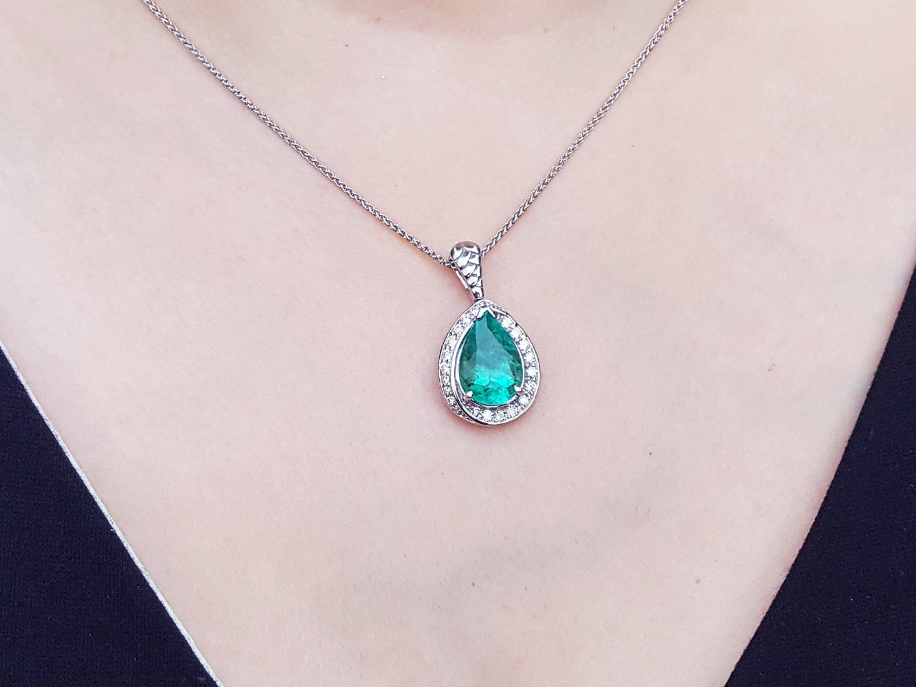 Emerald green teardrop pendant on a white gold chain against a neutral background