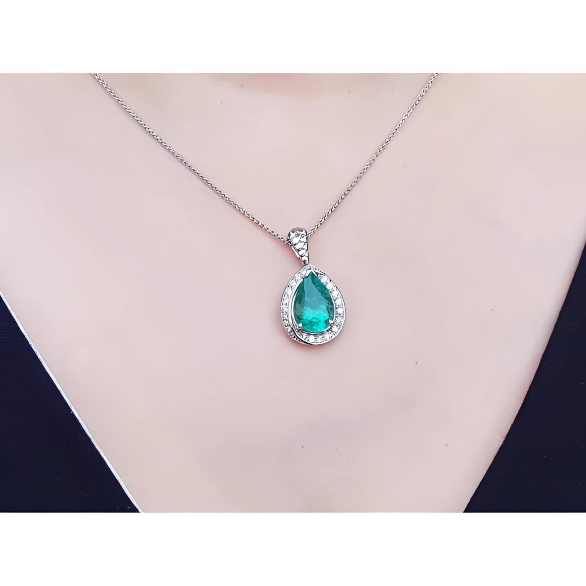 Pear-shaped natural emerald pendant with diamond halo on a 14K white gold chain, worn on a person.