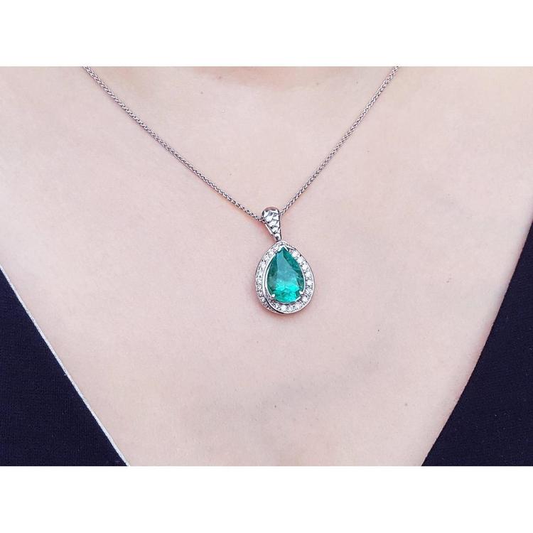 Pear-shaped natural emerald pendant with diamond halo on a 14K white gold chain, worn on a person.