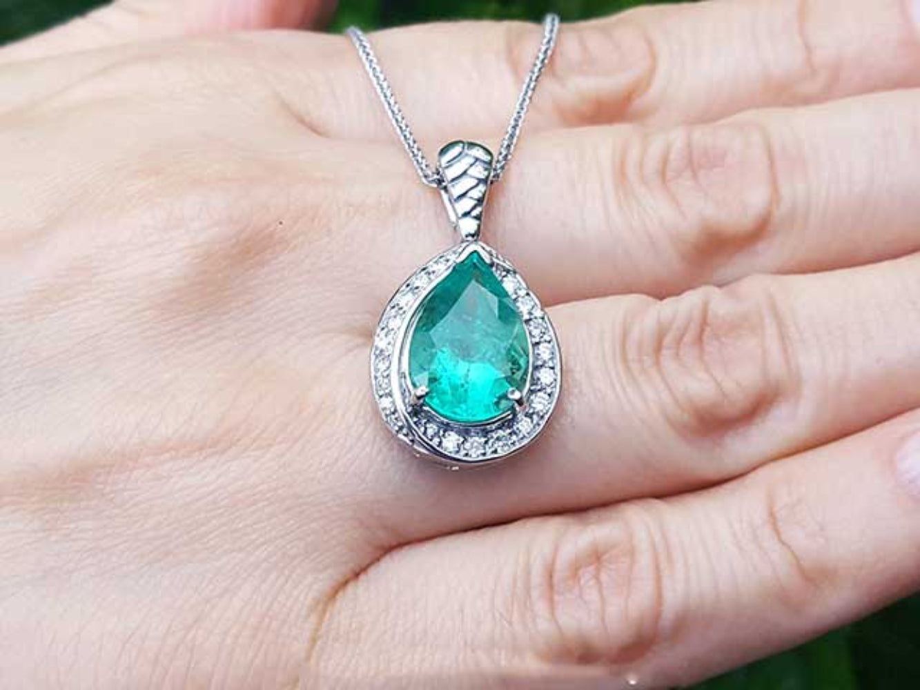 Green teardrop emerald pendant with white gold chain on a hand.