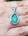 Green teardrop emerald pendant with white gold chain on a hand.