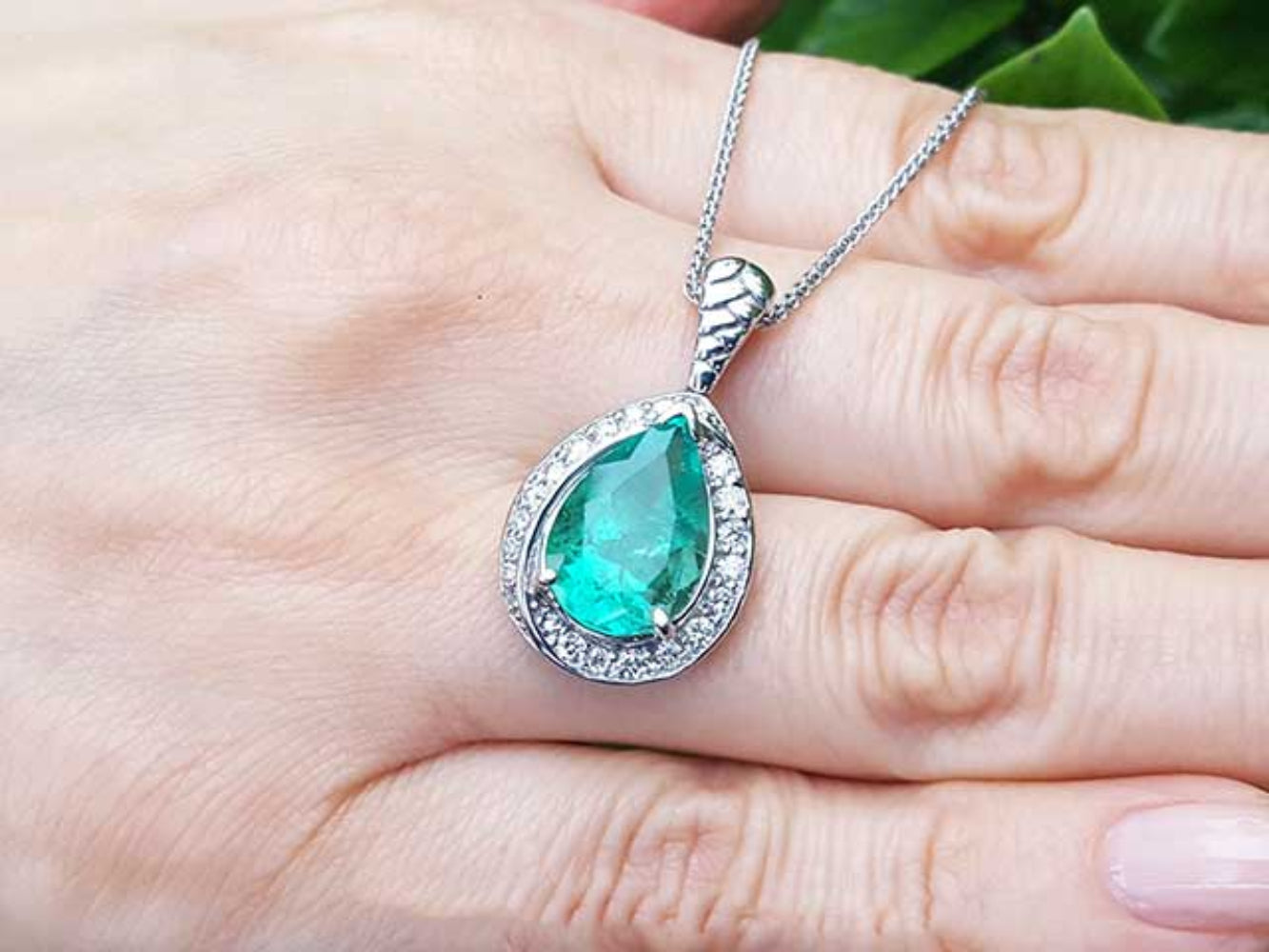Emerald green teardrop pendant on a white gold chain held in a hand.