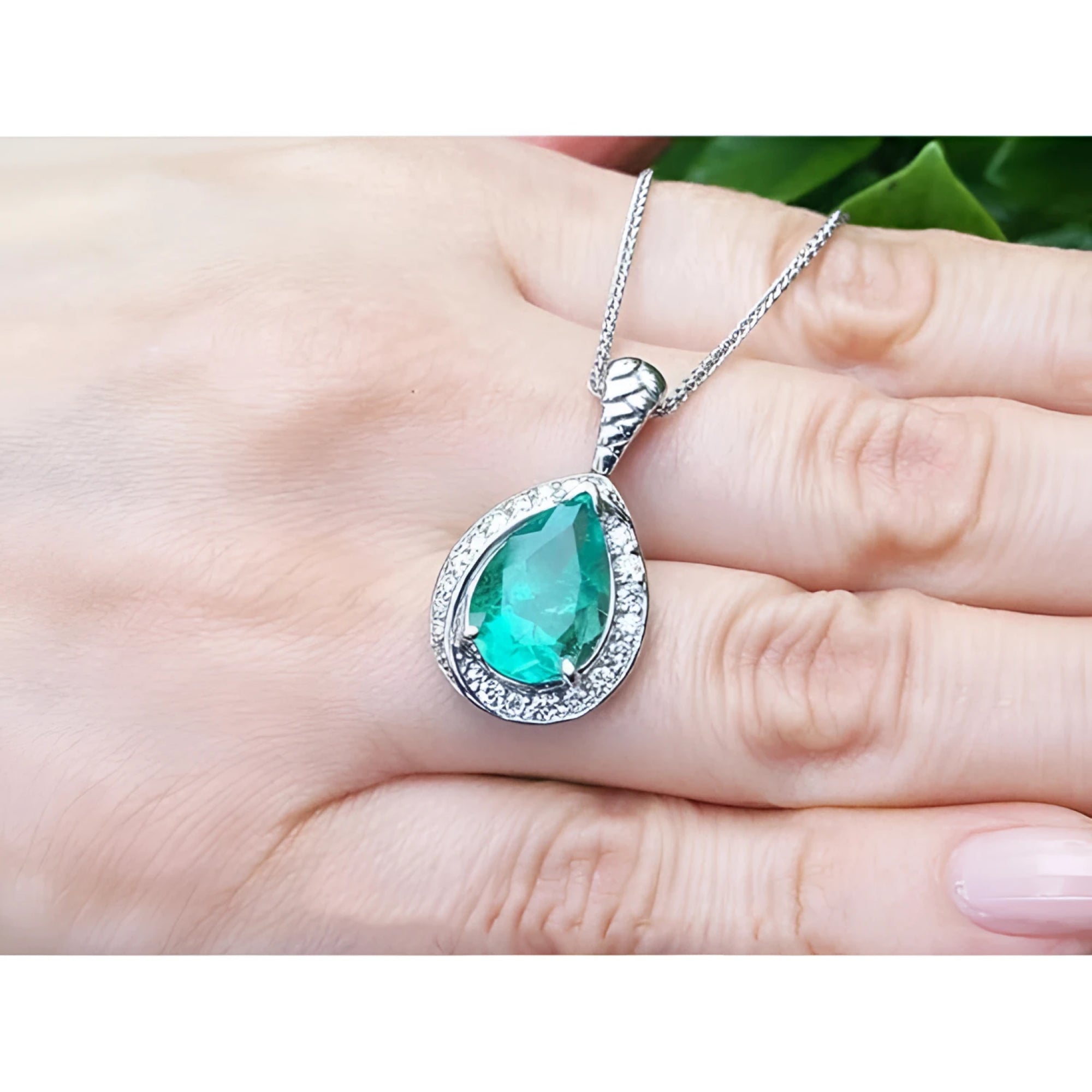 Pear-shaped natural emerald pendant with diamond halo on a 14K white gold chain, held by a hand.