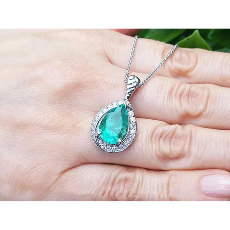Pear-shaped natural emerald pendant with diamond halo on a 14K white gold chain, held by a hand.