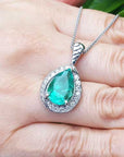 Emerald green teardrop pendant on a white gold chain held in a hand.
