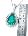 Pendant with pear cut emerald and white gold chain next to a ruler for size reference on a white background