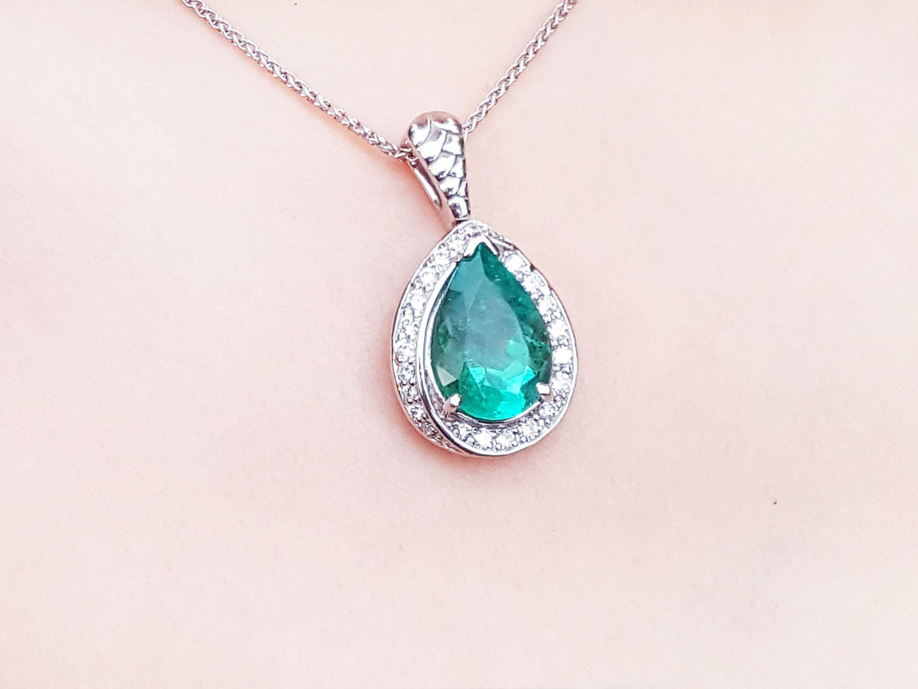 Emerald green teardrop pendant with diamonds on a skin background